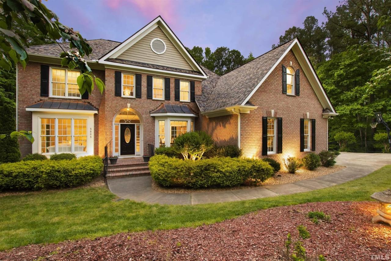A well-lit brick home with black shutters and white trim on a gorgeous wooded lot